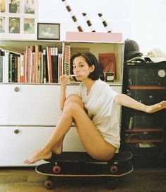 a woman sitting on top of a skateboard in front of a book shelf filled with books