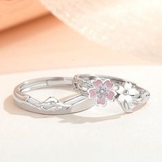 two silver rings with flowers on them sitting on a table next to a white cloth