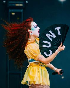 a woman with red hair and makeup holding a fan in front of her face while performing on stage