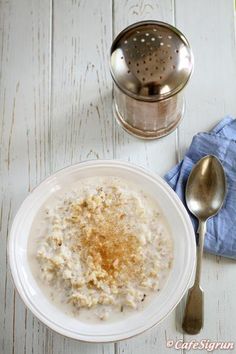 a bowl of oatmeal next to a strainer and spoon on a white table