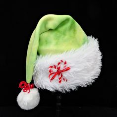 Novelty chartreuse, green tie dye soft poly fleece Santa hat is accented with a soft and fluffy faux fur fabric turn up brim with cotton fabric backing.  Brim is accented with a ribbon tied candy cane and rhinestone bow and there is a snowy white faux fur pompom dangle stitched on the top of the hat, accented with yarn tied red jingle bells. Hat is styled in the classic slouch stocking with generous sizing between 24-25" circumference and a length of 20". If you need additional quantity or a different size hat, send me a message as to availability. Green Santa, Green Tie Dye, Chartreuse Green, Fur Fabric, Rhinestone Bow, Green Tie, Faux Fur Fabric, Jingle Bell, White Faux Fur