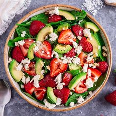 a salad with strawberries, avocado and feta cheese in a bowl