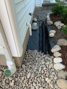 a drain in the side of a house with rocks around it and a water hose