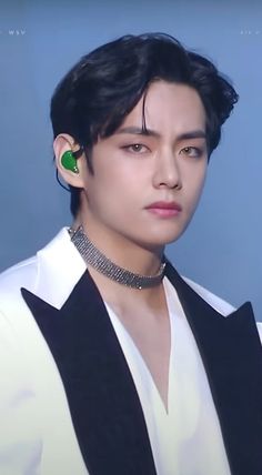 a young man with black hair wearing a white shirt and green earring