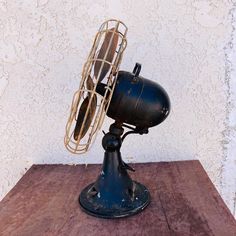 an old fashioned fan sitting on top of a wooden table next to a white wall