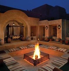 a fire pit in the middle of an outdoor area with seating and pillows on it