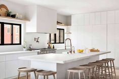 a kitchen with white counters and stools next to an island in front of windows