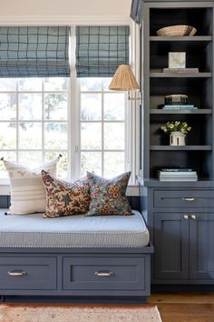 a window seat with pillows on it in front of a bookshelf