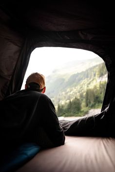 a man sitting in a tent looking out the window