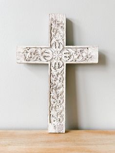 a white wooden cross sitting on top of a table next to a wall mounted clock