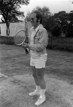 a man holding a tennis racquet on top of a grass covered field with trees in the background