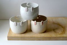 three white ceramic bowls with bunny ears on them sitting on a wooden board next to each other