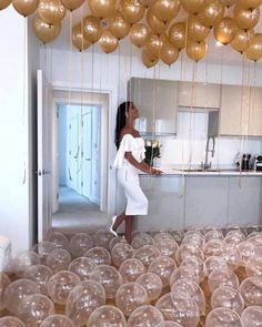 a woman standing in a kitchen surrounded by balloons