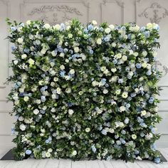 an artificial flower wall with blue and white flowers on the top, surrounded by greenery