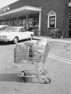 an old photo of a shopping cart in front of a store with cars parked on the street