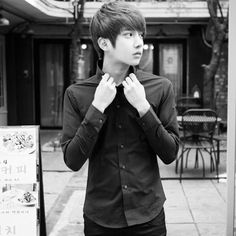 a young man standing in front of a building while tying his tie and looking at the camera