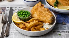 fish and chips with peas in a white bowl on top of newspaper next to silverware