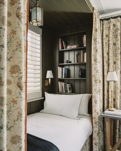 a bed sitting under a window next to a book shelf