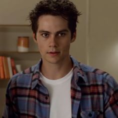 the young man is wearing a plaid shirt and standing in front of bookshelves