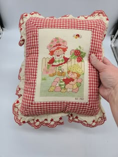 a hand holding a pillow that has a teddy bear on it and red gingham