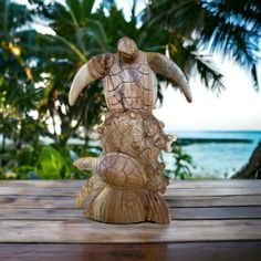 a wooden turtle statue sitting on top of a wooden table next to the ocean and palm trees