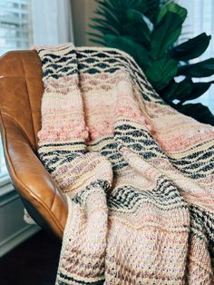 a chair with a blanket on it in front of a window and a potted plant