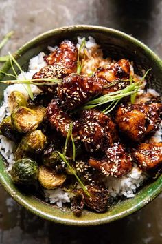 a green bowl filled with rice and meat covered in sesame seed sprinkles