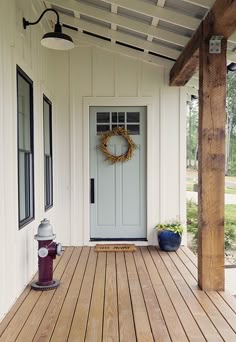 a porch with a fire hydrant and wreath on the front door, in front of a white house