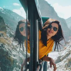 two women in sunglasses are looking out the window of a bus on a mountain road