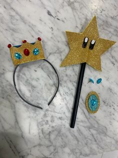 two paper crowns and a pencil on a marble counter top, one with blue eyes and the other has a gold star