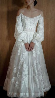 a woman in a white wedding dress standing next to a wooden wall with her hands on her hips