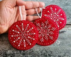 three red ornaments with white snowflakes on them are being held by someone's hand