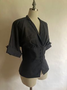 "1940s lightweight short sleeve jacket/blouse with pleated bust, covered buttons and lightly padded shoulders. Although the jacket appears to be black in the pictures, it is more of a slate grayMade by Wilshire of Boston, in excellent condition. The fabric is a bit of a mystery, it is lightweight with a striated texture, it could possibly be cotton or a form of rayon.  Shoulders 17\" across Chest 42\" (21\" across, doubled) Waist 34\" Hem 42\" Sleeve from neck to rolled cuff16\" Length from back of neck to hem 23\"" Elegant Single Breasted Tops, Classic Short Sleeve Outerwear For Formal Occasions, Classic Short Sleeve Outerwear For Formal Events, Fitted Blouse With Lapel Collar And Hidden Buttons, Fitted Blouse With Lapel Collar And Buttons, Fitted Blouse With Buttons And Lapel Collar, Tailored Short Sleeve Formal Tops, Fitted Collared Blouse With Hidden Button Closure, Single Breasted Fitted Top With Lapel Collar