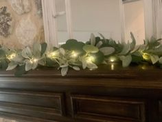 a mantle with some green leaves and lights on it