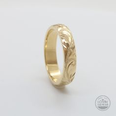 a gold wedding ring with an intricate design on the outside and inside, sitting on a white surface