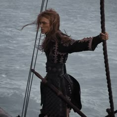 a woman dressed in black standing on the deck of a boat