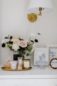 flowers and candles sit on a white table with gold trim around the edges, along with framed pictures