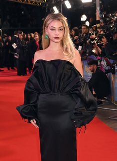 a woman standing on top of a red carpet wearing a black dress and green earrings