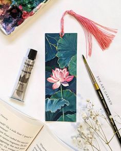 a bookmark with a pink flower on it next to some watercolors and paint