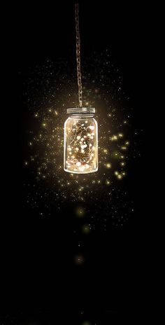 a mason jar hanging from a chain on a dark background with lights in the air