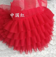 a red tutu skirt sitting on top of a white lace tablecloth next to a stuffed animal