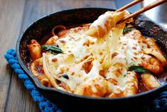 a skillet filled with pasta and cheese being held by chopsticks