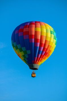 a multicolored hot air balloon flying in the blue sky with a person inside