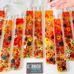 seven glass tubes with different colored flowers on them and one being held by a person's hand