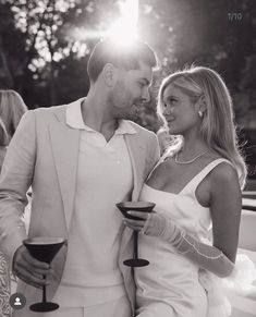 a man and woman standing next to each other holding wine goblets in their hands