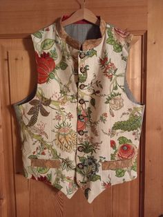 a white vest with flowers and leaves on it hanging from a wooden door knobs