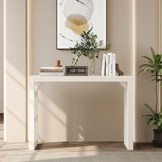 a white table with books and plants on it in front of a large painting hanging on the wall