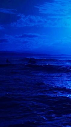 two surfers are riding the waves in the dark blue ocean at night with full moon behind them