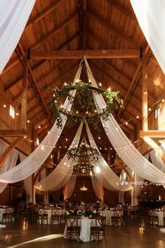 the inside of a barn decorated with white drapes and greenery hanging from the ceiling