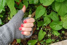 a woman's hand with red and white nail polish holding onto a gray knitted mitt